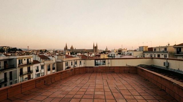 An empty terracotta-tiled rooftop overlooking a city skyline in soft evening light.