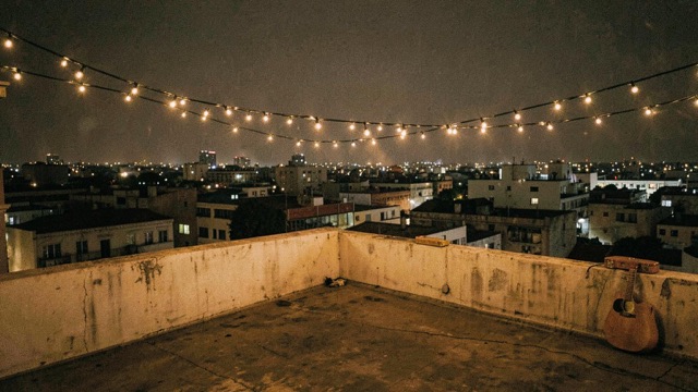 An empty city rooftop at night beneath strings of warm lights.