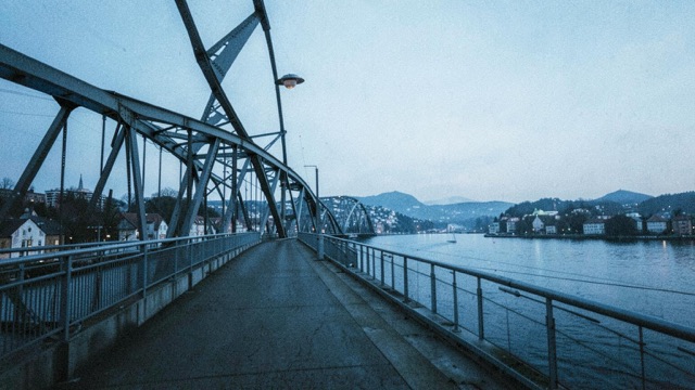 An empty steel bridge crossing water beneath a cool blue sky.