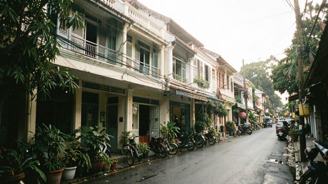 A quiet street lined with low-rise shophouses, balconies and leafy plants.